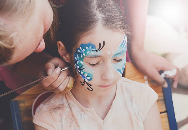 Female child face painting, making butterfly process Child animator, artist's hand draws face painting to little girl. Child with funny face painting. Painter makes blue butterfly at girl's face. Children holiday, event, birthday party, entertainment. face paint stock pictures, royalty-free photos & images