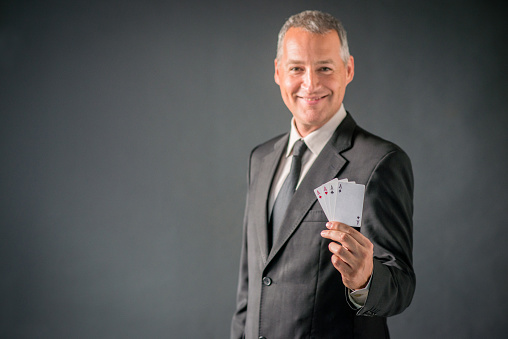 Businessman Showing Card Hand of Aces, Man in dark suit with necktie showing poker of aces over gray background