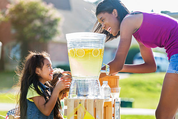Happy girls sell lemonade to adult customer Little girls smile while serving lemonade to African American customer. The customer smiles at the girls while they serve her. images of lemonade stands stock pictures, royalty-free photos & images
