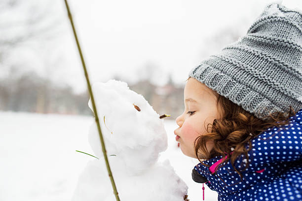 niña besando a un muñeco de nieve en la naturaleza invernal - snowman snow winter fun fotografías e imágenes de stock