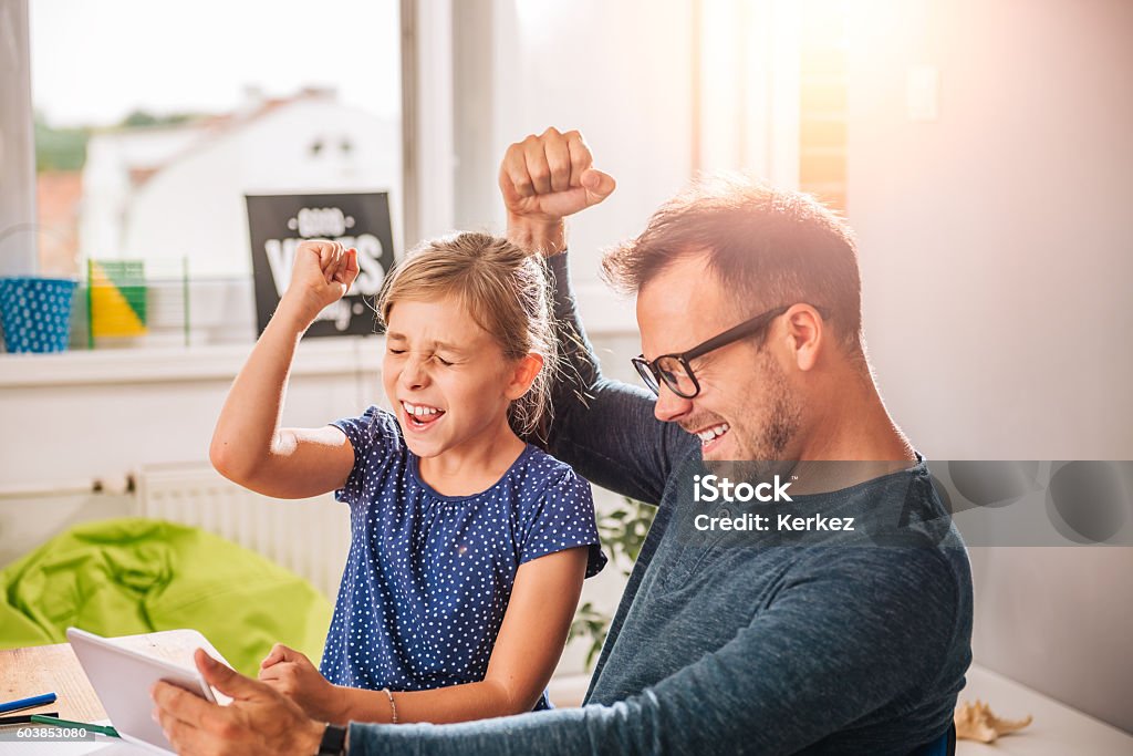 Father And Daughter Cheering during playing game on tablet Homework Stock Photo