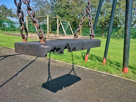 Damaged black moulded plastic swing seat and rusty chains in a rural park playground.