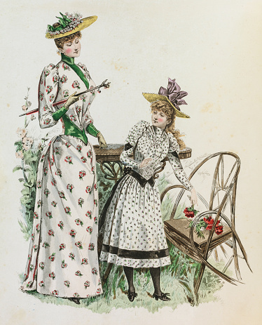 Two women showing dresses in floral  pattern with queue de Paris and lace collar and a teenage girl in a dress with high heel black shoes with roses on the chair