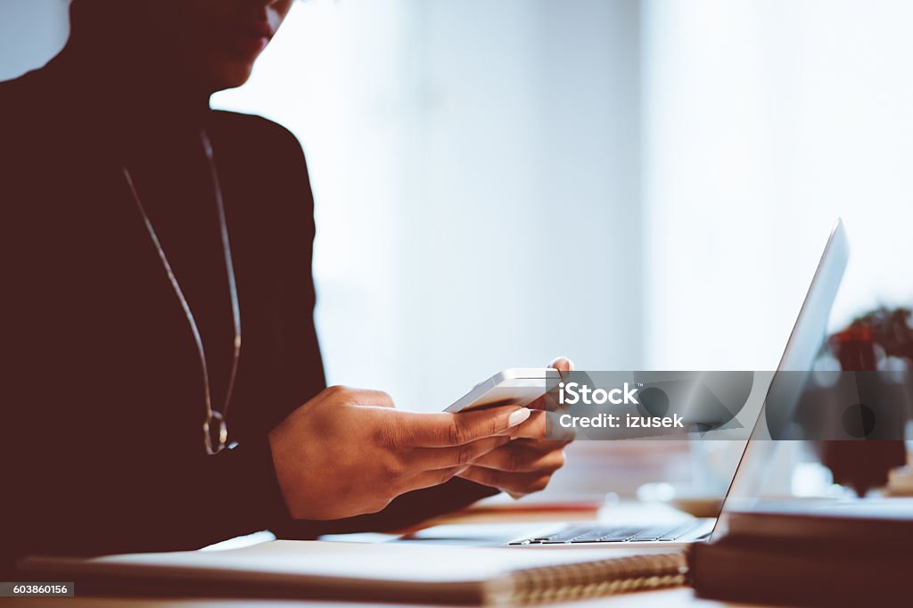 Elegance woman using mobile in an office or at home Elegance young woman texting on smart phone in an office or at home, focus on hands, unrecognizable person. Adult Stock Photo
