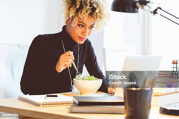 Afro American Young Woman Eating Lunch At The Desk Stock Photo - Download Image Now - Lunch, Laptop, Office
