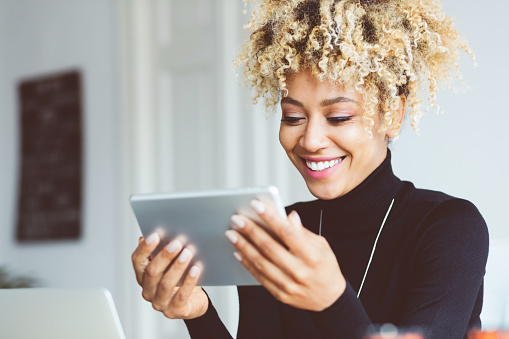 Beautiful afro american young woman using a digital tablet in an office, receiving good news, smiling. Close up of face.