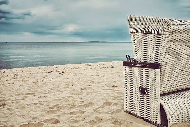 Retro stylized hooded wicker basket chair on an empty beach.