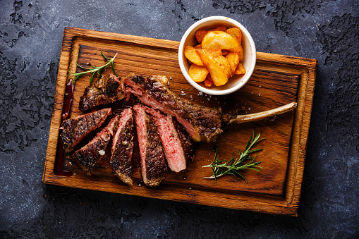 Sliced Medium rare barbecue Steak on bone Veal rib with potato wedges on dark background