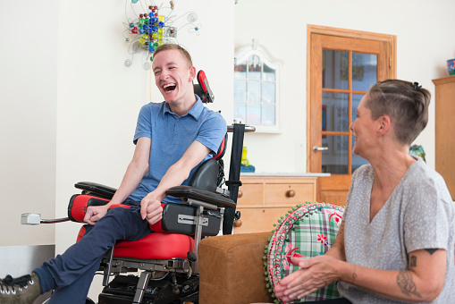 Color image of a real life young physically impaired ALS patient spending time with his mother at home. He is happy.