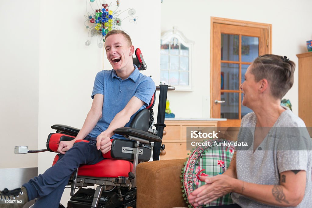 Happy young ALS patient with his mom Color image of a real life young physically impaired ALS patient spending time with his mother at home. He is happy. Disability Stock Photo