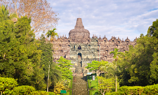 Java Borobudur temple front view panorama with the central stairs and surrounding vegetation on a sunny day.