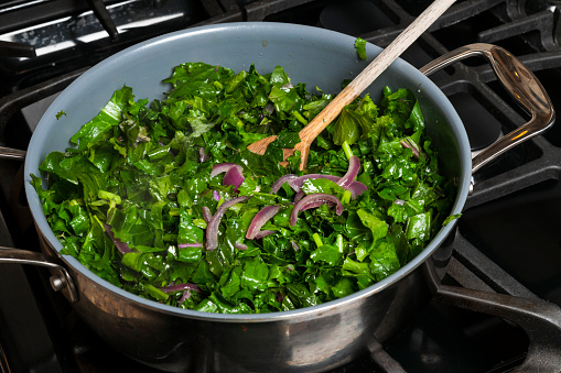 Fresh kale sauteed with onions in a cooking pan on gas stove