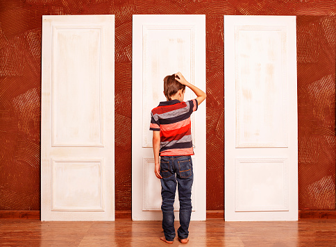 doubting boy stands in front of three closed doors. view from the back