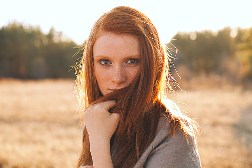 Young Woman with Red Hair in Golden Field at Sunset.