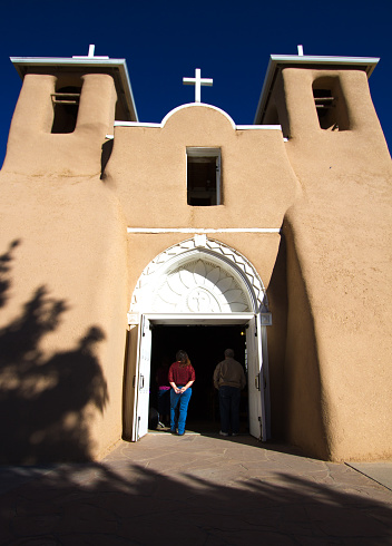 Taos, NM, USA - September 11, 2016: Front view of Ranchos de Taos church (San Francisco de Asis Mission Church) in early morning light, with parishioners standing in the doorway. The adobe church was completed in 1816 and is located near Taos, New Mexico. 
