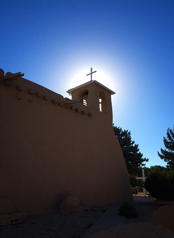 Ranchos de Taos church (San Francisco de Asis Mission Church) silhouetted in dramatic early morning sun.  There is a sun halo around the bell tower. Completed in 1816, the adobe church is located just outside Taos, New Mexico.