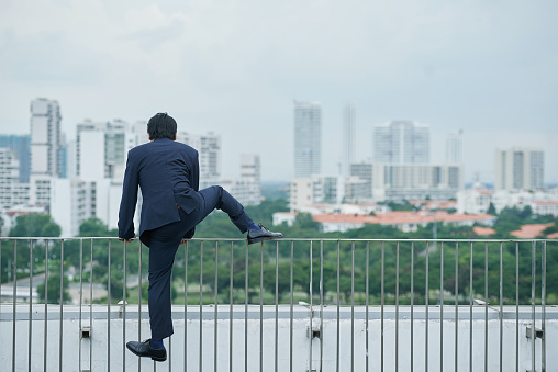 Businessman climbing over barrier on rooftop, rear view