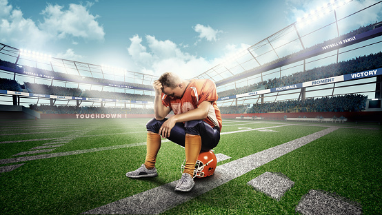 Professional american football player sitting on helmet green grass