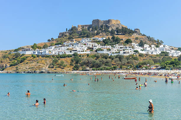 Rhodes, Greece - June 24, 2016: Lindos beach with Acropolis in the background. Photo taken during a hot summer day from the boat dock on the beach.