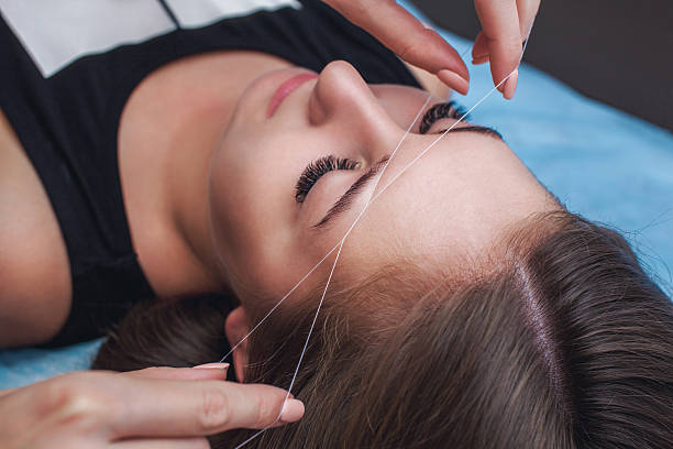 Master in the cabin removes facial hair strand. Master corrects makeup, gives shape and thread plucks eyebrows in a beauty salon. Professional care for face and eyebrows. thread sewing item photos stock pictures, royalty-free photos & images