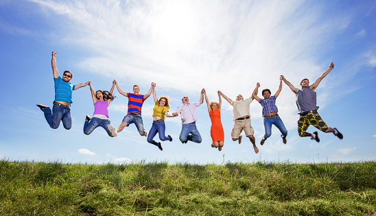 Large group of happy people in nature jumping high up while holding hands and looking at camera. Copy space.