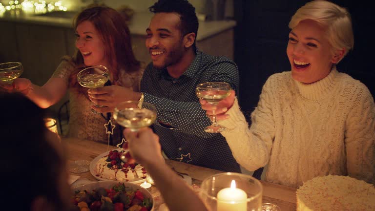Friends toasting champagne glasses at candlelight table with Christmas desserts. MS, RL pan, slow motion.