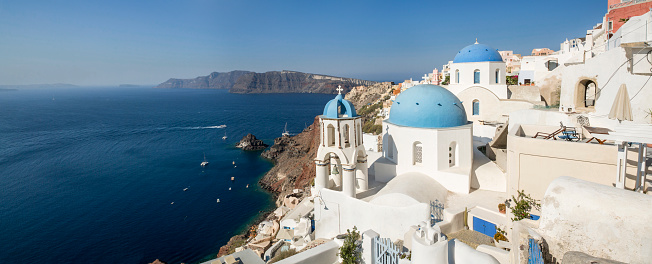 Early morning view of the village of OIA facing the volcanic caldera in Santorini, a place famous worldwide for the iconic church and bell tower painted in white with their light blue dome. Santorini in Greece is one of the most famous travel destination with numerous cruise ships anchoring in the bay below.