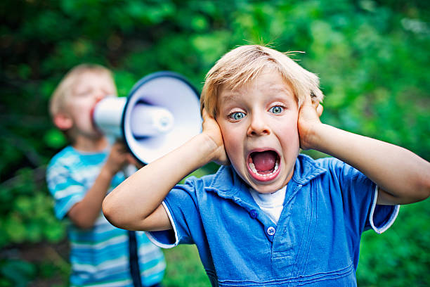 Little boy being yelled on by his brother Little boy covering his ears while his brother is yelling on him with megaphone. hands covering ears stock pictures, royalty-free photos & images