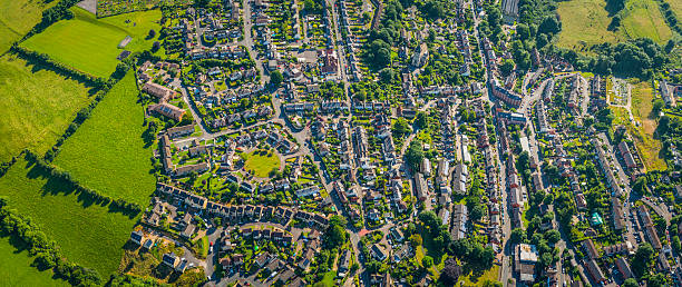 Aerial panorama over suburban homes gardens streets housing green fields Aerial view over homes, streets and suburban community at the edge of a country town surrounded by green pasture and farmland, Stroud, UK. gloucestershire stock pictures, royalty-free photos & images