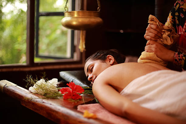 Spa Therapist Treating Female therapist treating a young lady in an ayurvedic spa following Indian traditional method. ayurveda stock pictures, royalty-free photos & images