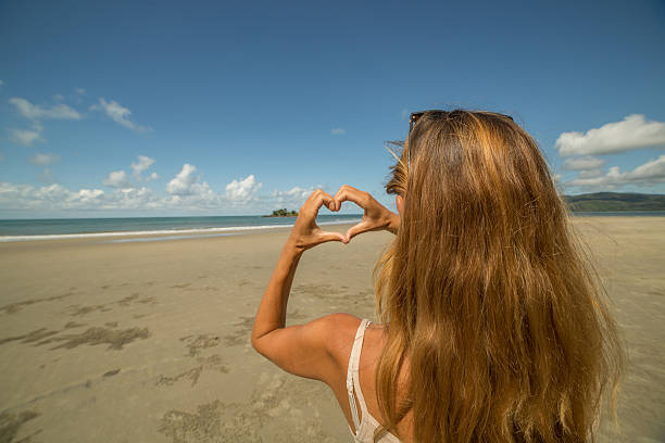 istock Young woman on beach makes a heart shape finger frame 604006122