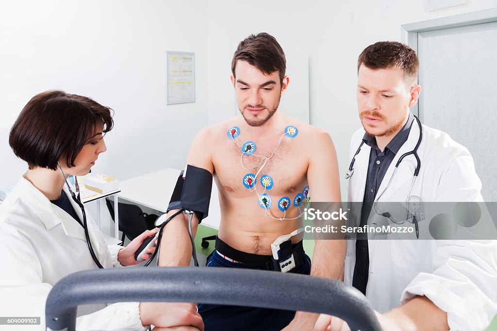 interpretation of the electrocardiogram of young athlete Athlete does a cardiac stress test in a medical study, monitored by the doctor and nurse Electrocardiography Stock Photo