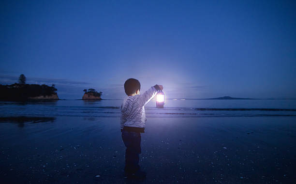 Boy with Lantern in his hand. Boy holding lantern in his hand and looking towards beach. could be waiting for someone or a metaphor of hope or spirituality. auckland region photos stock pictures, royalty-free photos & images