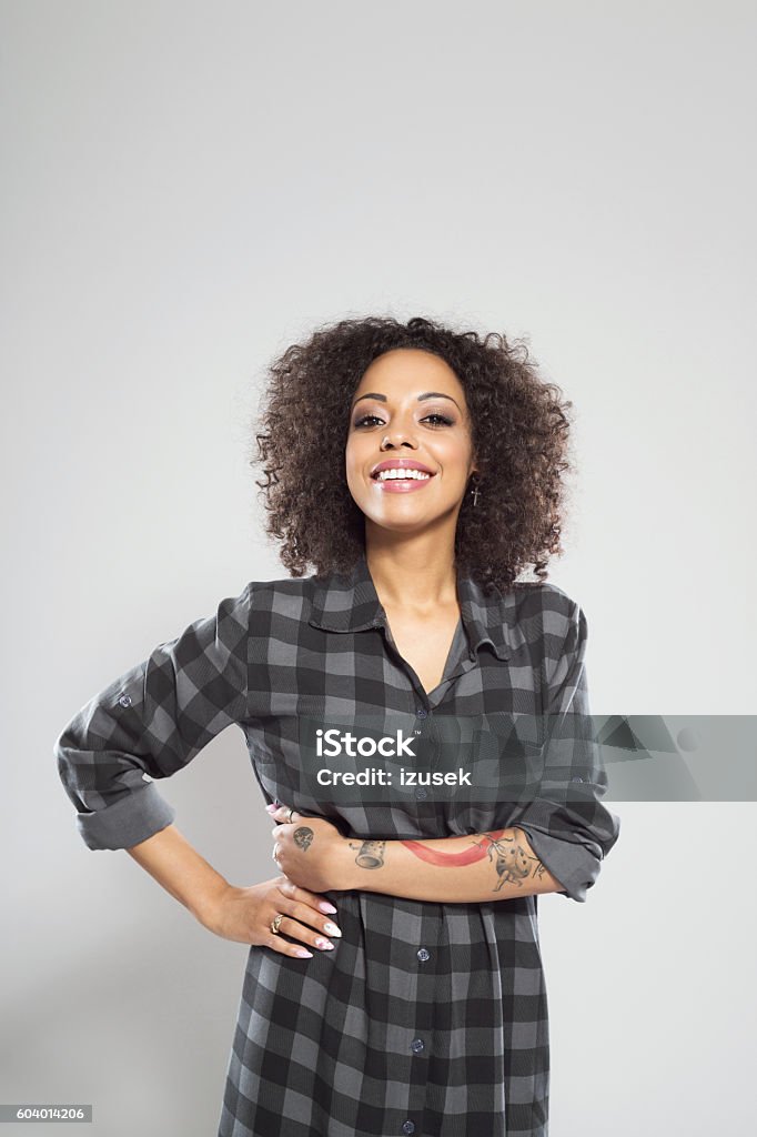 Portrait of happy afro american young woman Portrait of happy afro american young woman wearing casual checkered dress, standing against grey background, laughing at camera. Adult Stock Photo