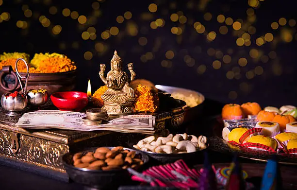 oil lamp or diya with crackers, sweet or mithai, dry fruits, indian currency notes, marigold flower and statue of Goddess Laxmi on diwali night