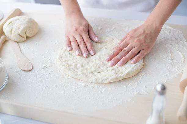 istock Woman kneading pizza dough on wooden pastry board. 604016574
