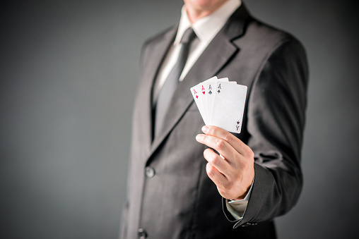 Photo of Businessman Showing Card Hand of Aces, Man in dark suit with necktie showing poker of aces over gray background