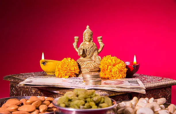 oil lamp or diya with crackers, sweet or mithai, dry fruits, indian currency notes, marigold flower and statue of Goddess Laxmi on diwali night