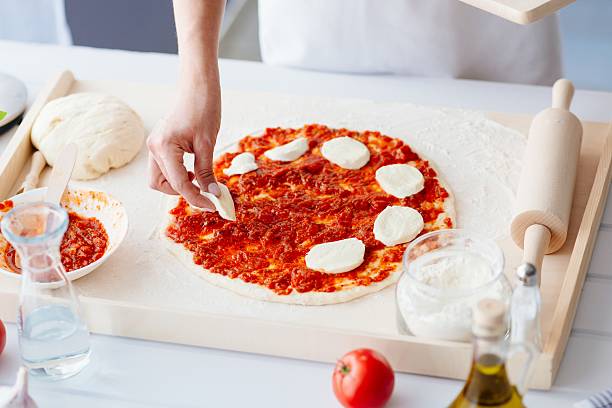 istock Woman puts slices of mozzarella on the pizza 604017672
