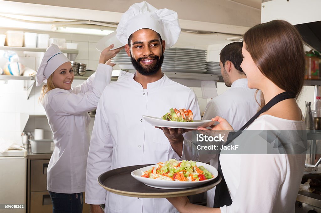 Waitress and crew of professional cooks posing at restaurant european waitress and crew of professional cooks posing at restaurant kitchen Adult Stock Photo