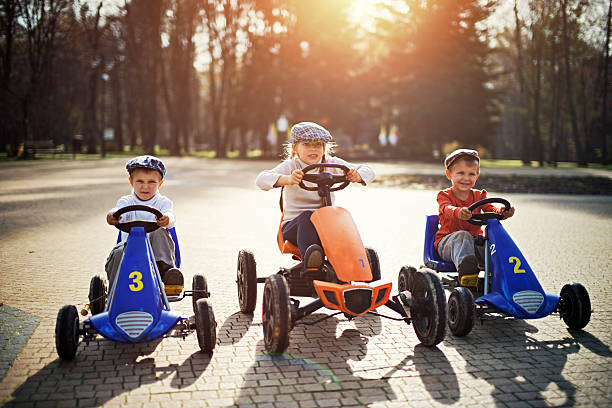 Kids getting ready to retro go-kart race Three kids getting ready to start in a retro go-kart race. Gids are grabbing the steering wheels and focusing.  Sunny day. soapbox cart stock pictures, royalty-free photos & images