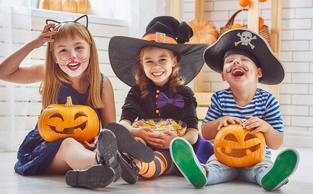 children play with pumpkins Happy brother and two sisters on Halloween. Funny kids in carnival costumes indoors. Cheerful children play with pumpkins and candy. candy house stock pictures, royalty-free photos & images