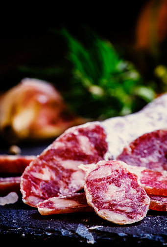 Jerked Italian salami with rosemary, spices, olives and oil. Dark vintage background, low key, selective focus