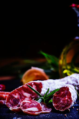 Jerked Italian salami with rosemary, spices, olives and oil. Dark vintage background, low key, selective focus