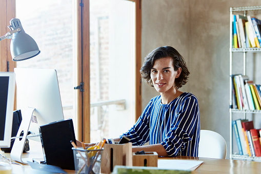 Portrait of confident young businesswoman sitting at desk in creative office