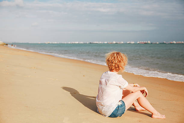 istock Woman Sitting On Beach Against Cloudy Sky 604222457
