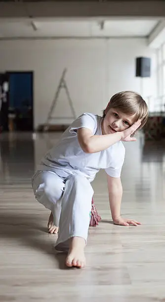 Cute boy in white clothes practicing capoeira (brazilian martial art that combines elements of dance, acrobatics and music)  in gym