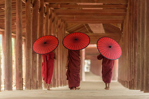 Three Buddhist novices with red umbrella on their shoulder are walking inside pagoda in Mandalay Myanmar