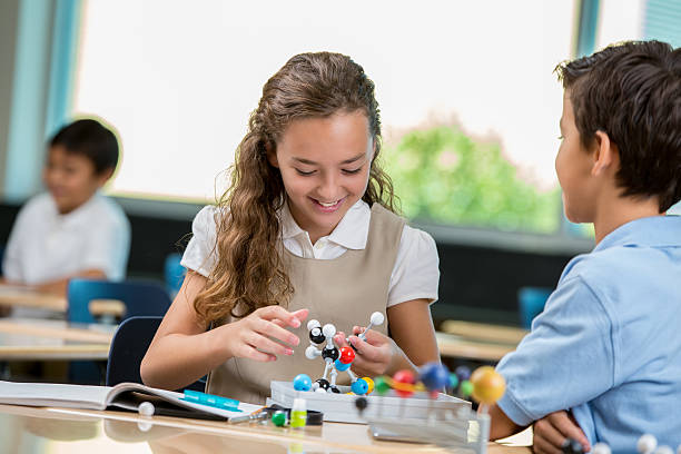 istock Smiling elementary schoolgirl works on science project 604338778
