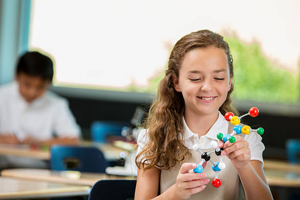 istock Cheerful little girl works with molecular structure model in class 604338796